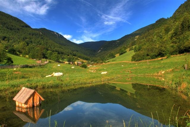 A small pond in a green mountain landscape with a blue sky.