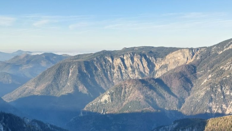View of a deep gorge with steep rock faces and wooded mountains in the background under a clear sky.