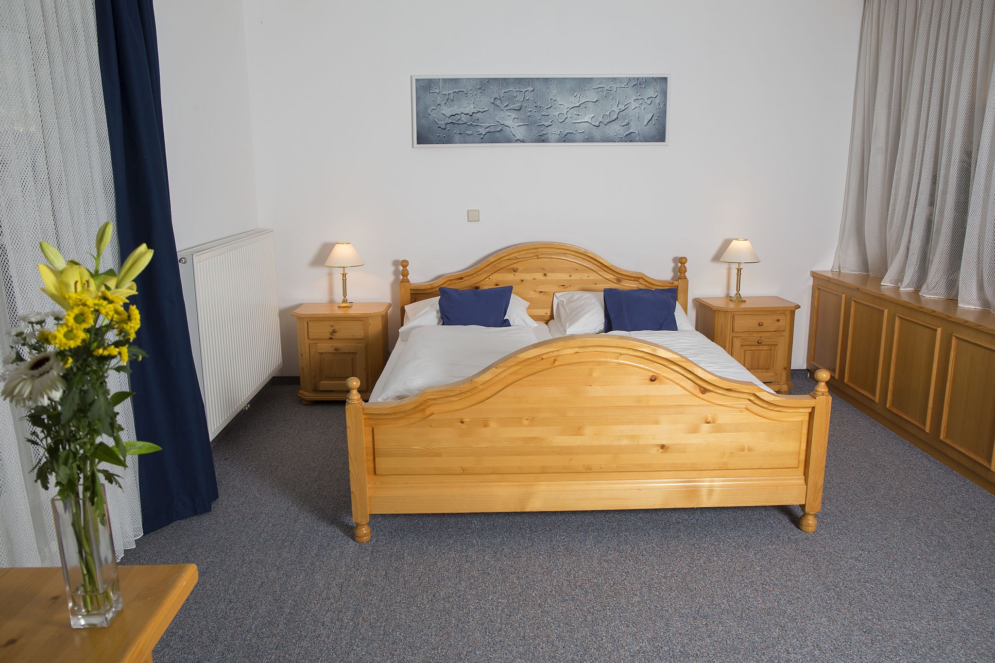 A bedroom with a wooden double bed, two bedside tables with lamps and a bouquet of flowers on a table.