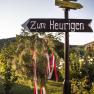 A signpost with the inscription 'Zum Heurigen' points in one direction. Trees and flowers can be seen in the background.