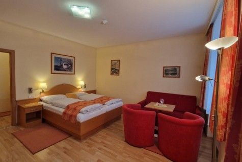 Hotel room with double bed, red sofa and armchairs, wooden floor and murals.