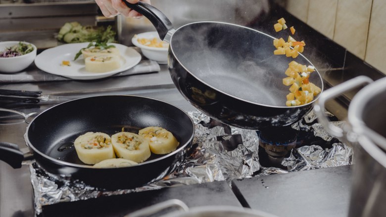 Cook tosses vegetables in a pan on a stove.