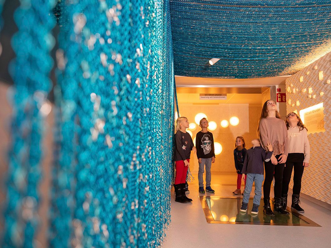 Children stand in a room with blue, hanging nets and illuminated walls.