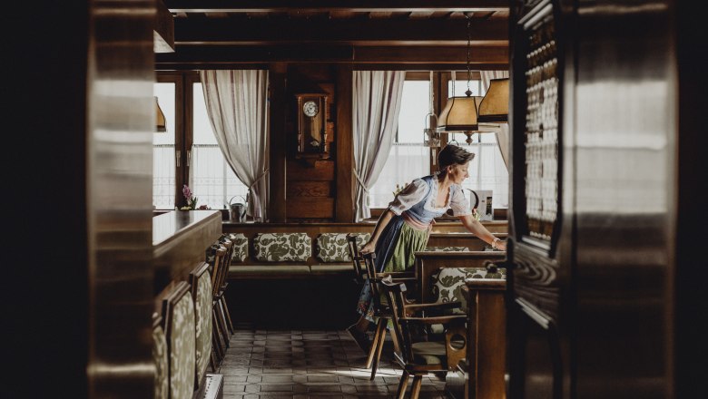 A woman in traditional dress prepares a table in a cozy, wood-paneled dining room.