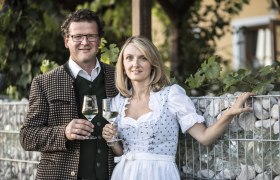 A man and a woman in traditional dress are holding wine glasses.