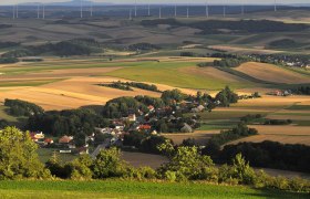 Landscape with fields, a village and wind turbines in the background.