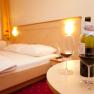 A cozy hotel room with a double bed, two wine glasses and a bottle of wine on a table.