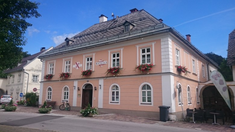 A two-storey, pink building with white window frames and flower boxes, labeled 'Rathaus'.