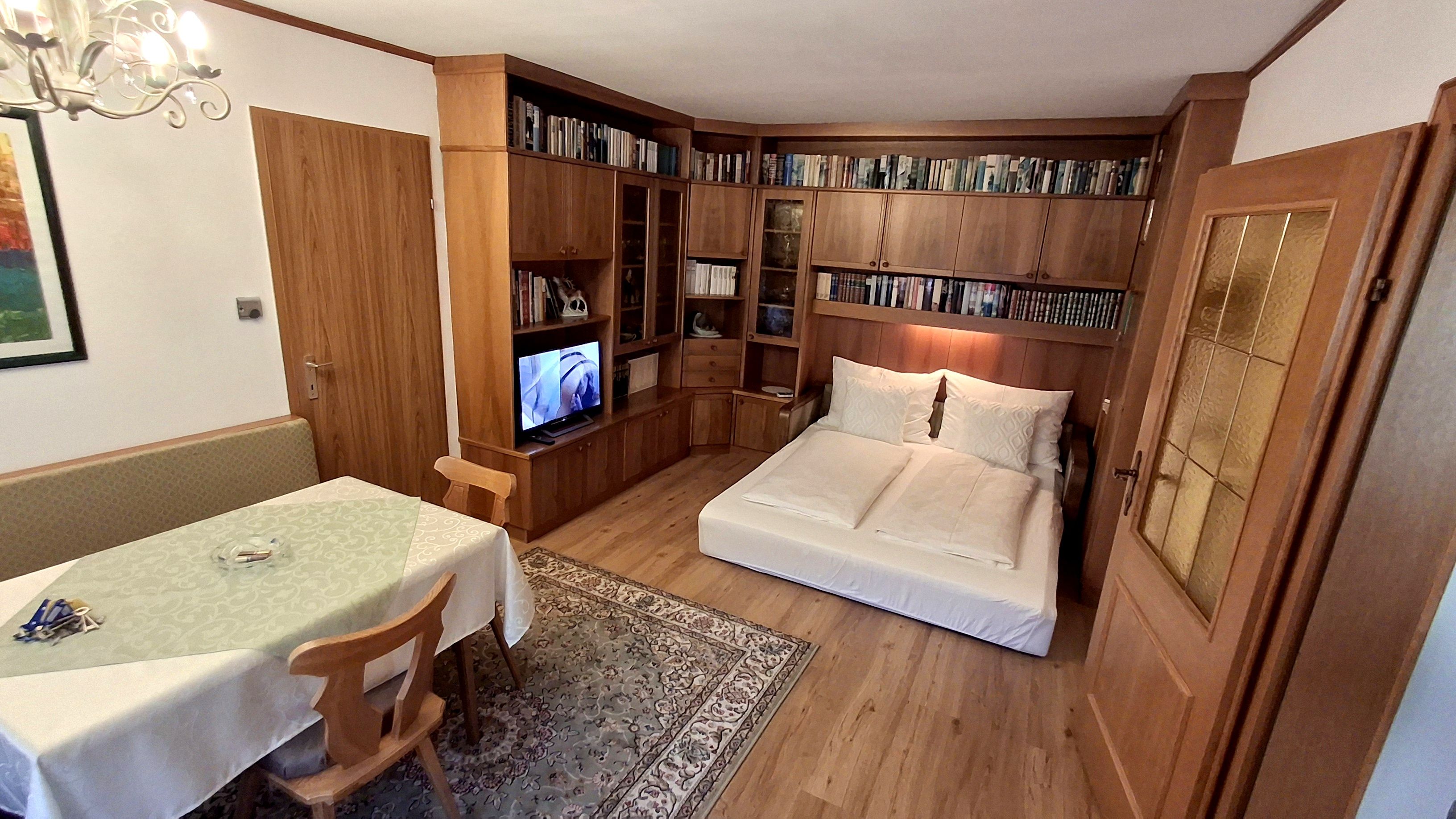 Living room with pull-out couch, bookshelf, dining table and TV.