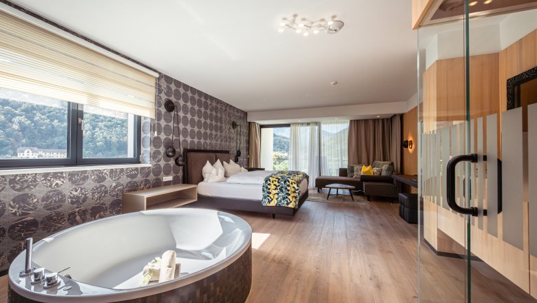 Luxurious hotel room with free-standing bathtub, large bed and panoramic window with a view of nature.