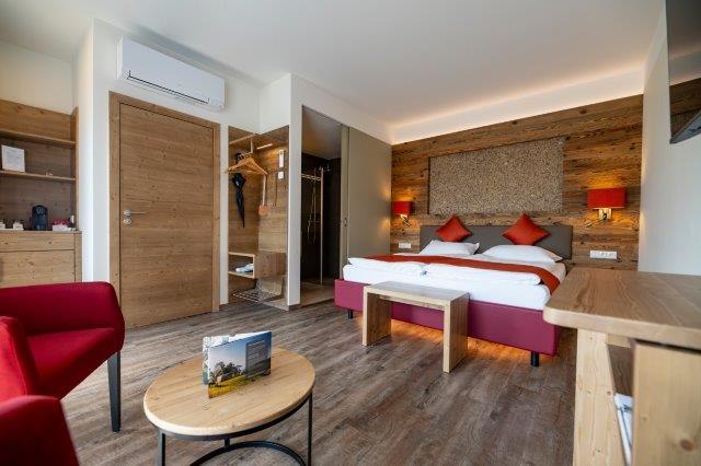 Modern guest room with double bed, wooden furniture and red accents.