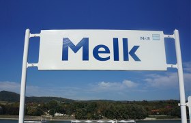 Sign with the inscription 'Melk Nr. 8' in front of a blue sky.