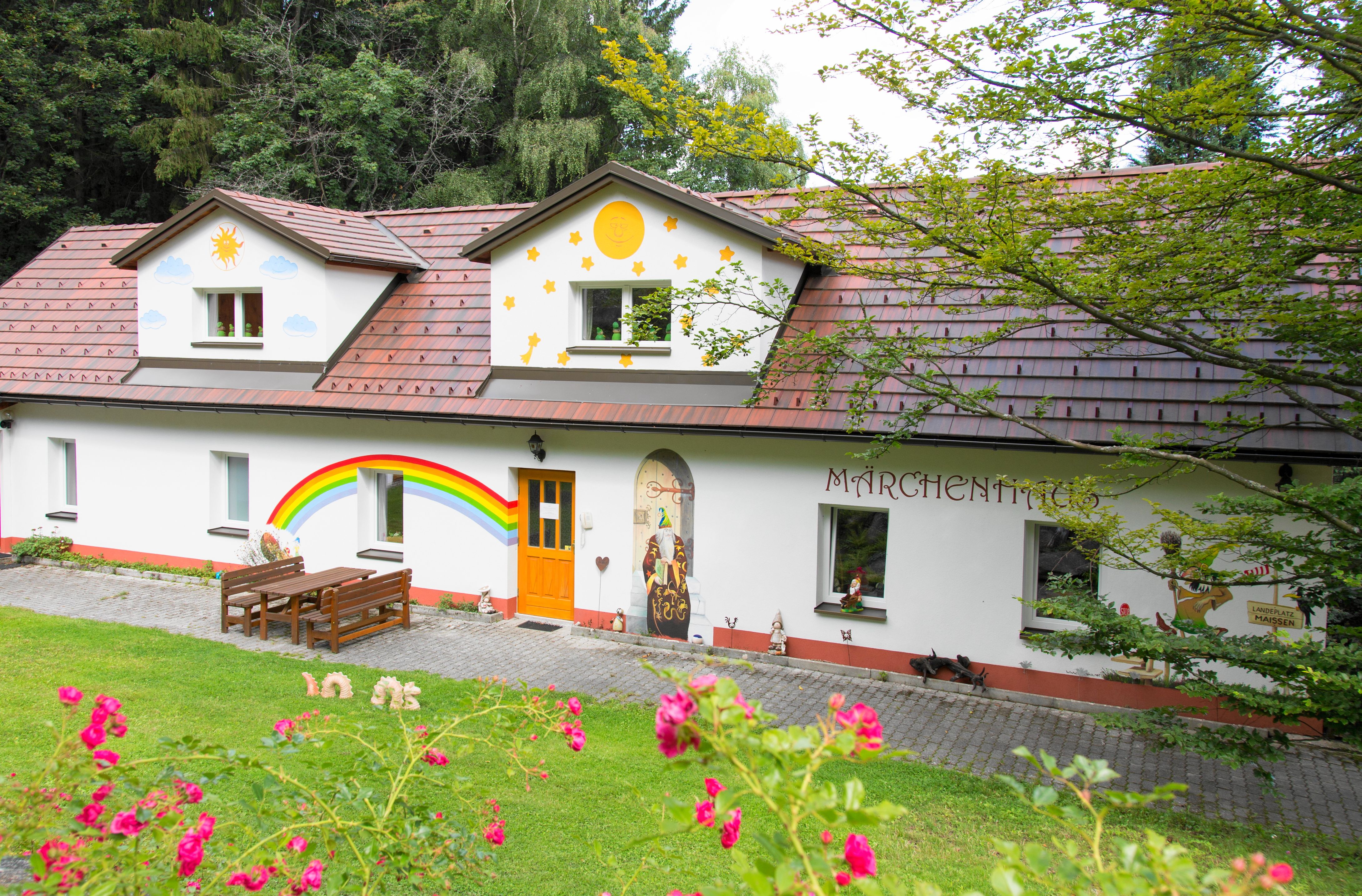 A colorfully painted house with fairytale motifs and a rainbow on the wall, surrounded by green nature.