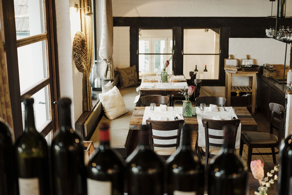 Cozy restaurant with wooden tables and bottles of wine in the foreground.