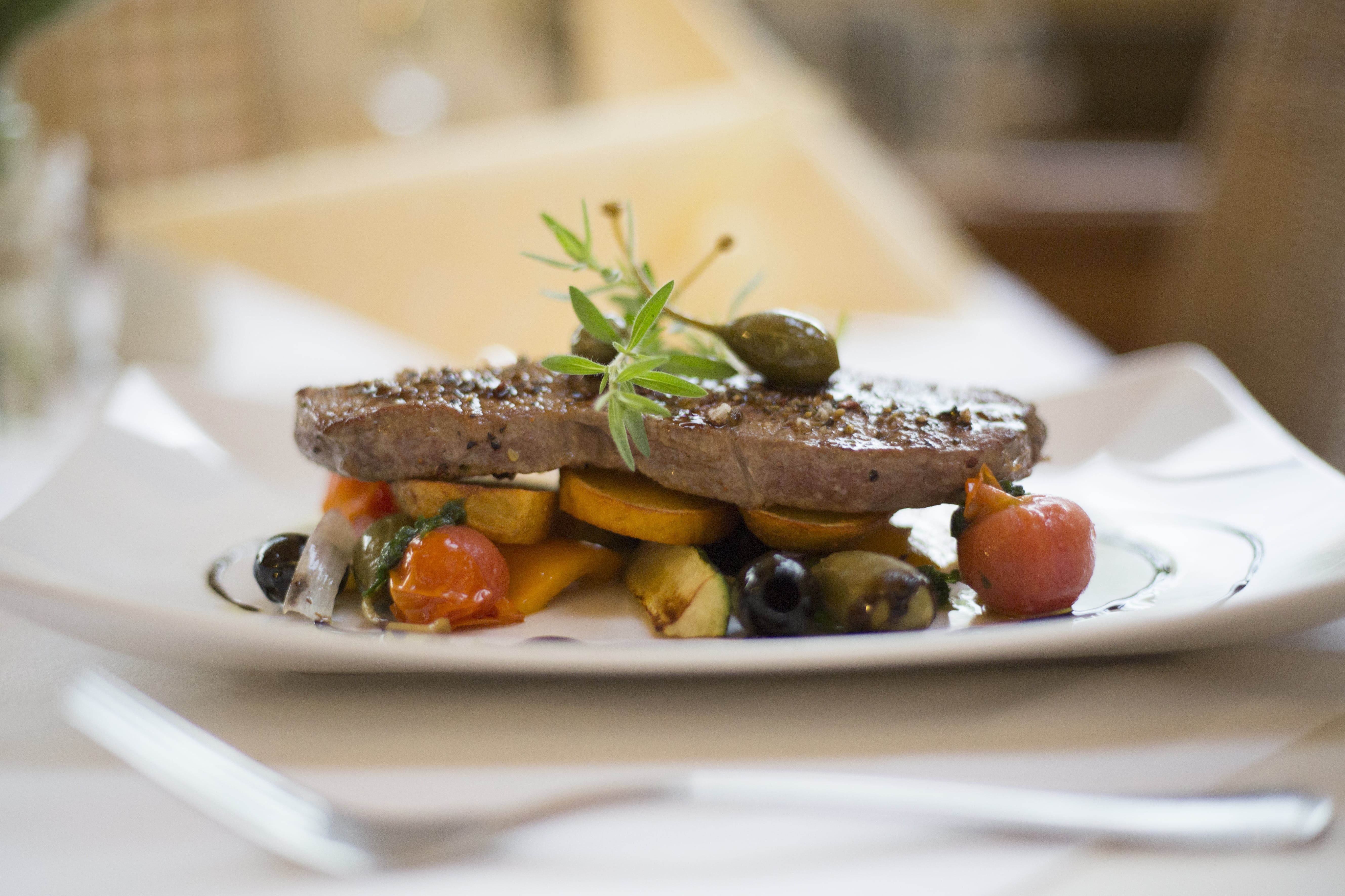 A plate with a piece of meat, garnished with vegetables and herbs.