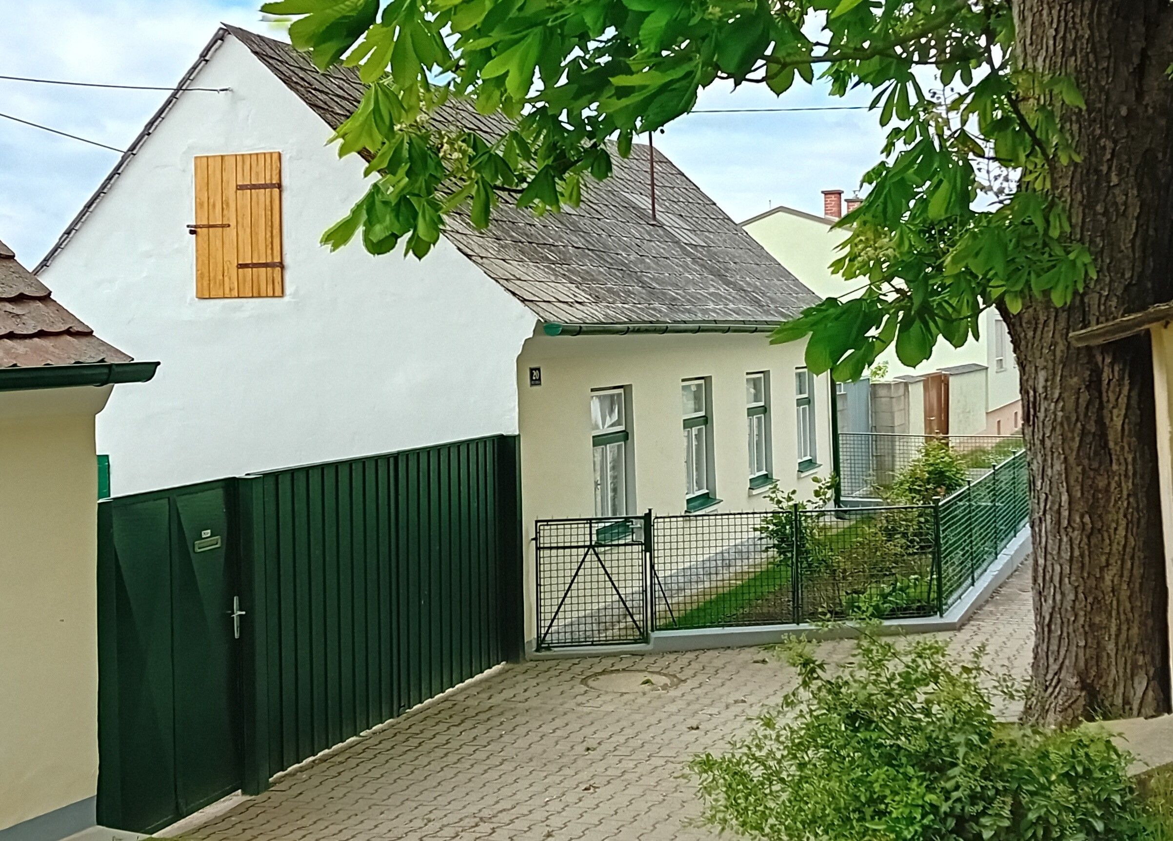 A traditional white cottage with a green fence and tree in the foreground.