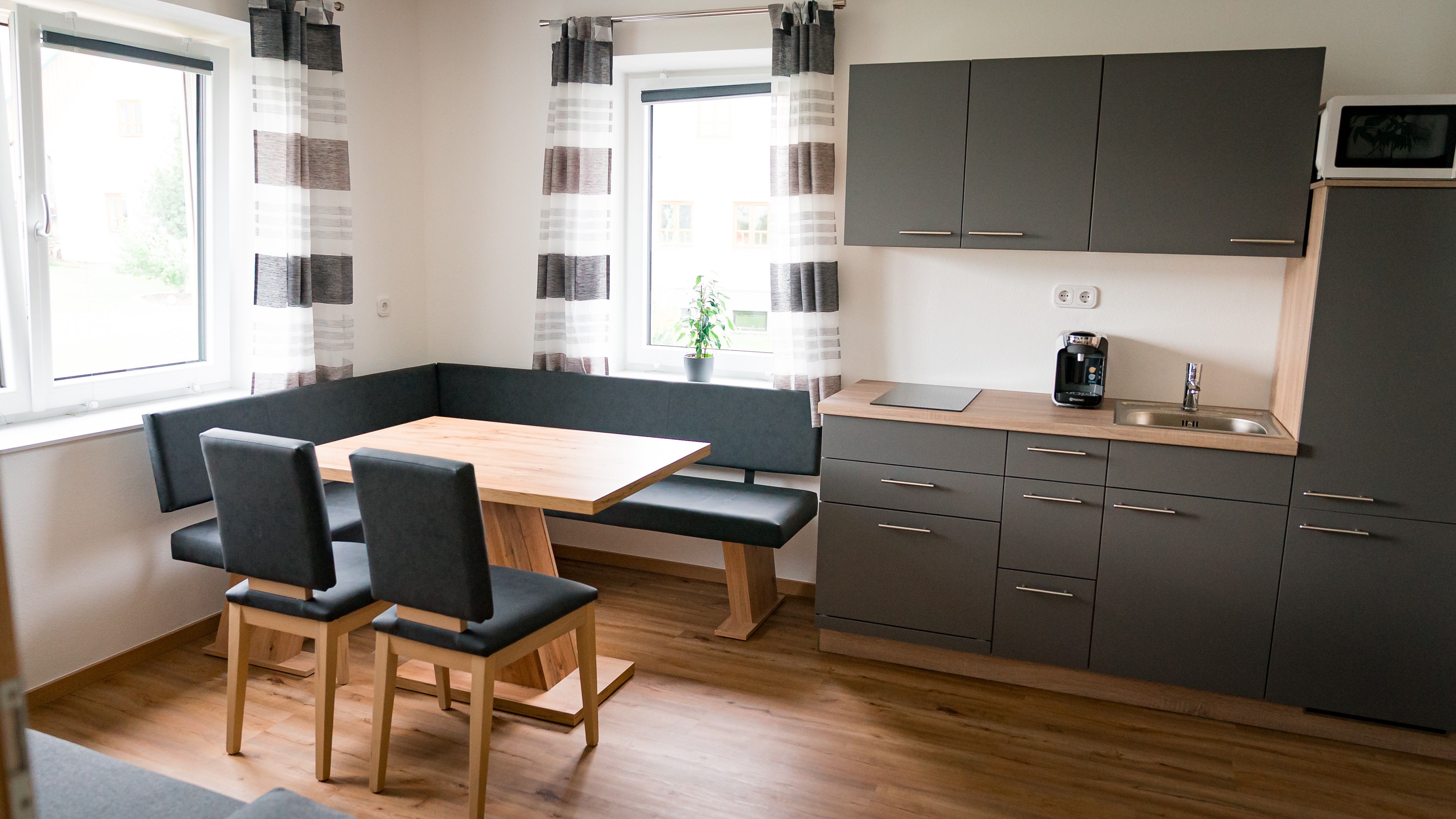 Modern kitchen with gray cabinets, wooden table and corner bench.