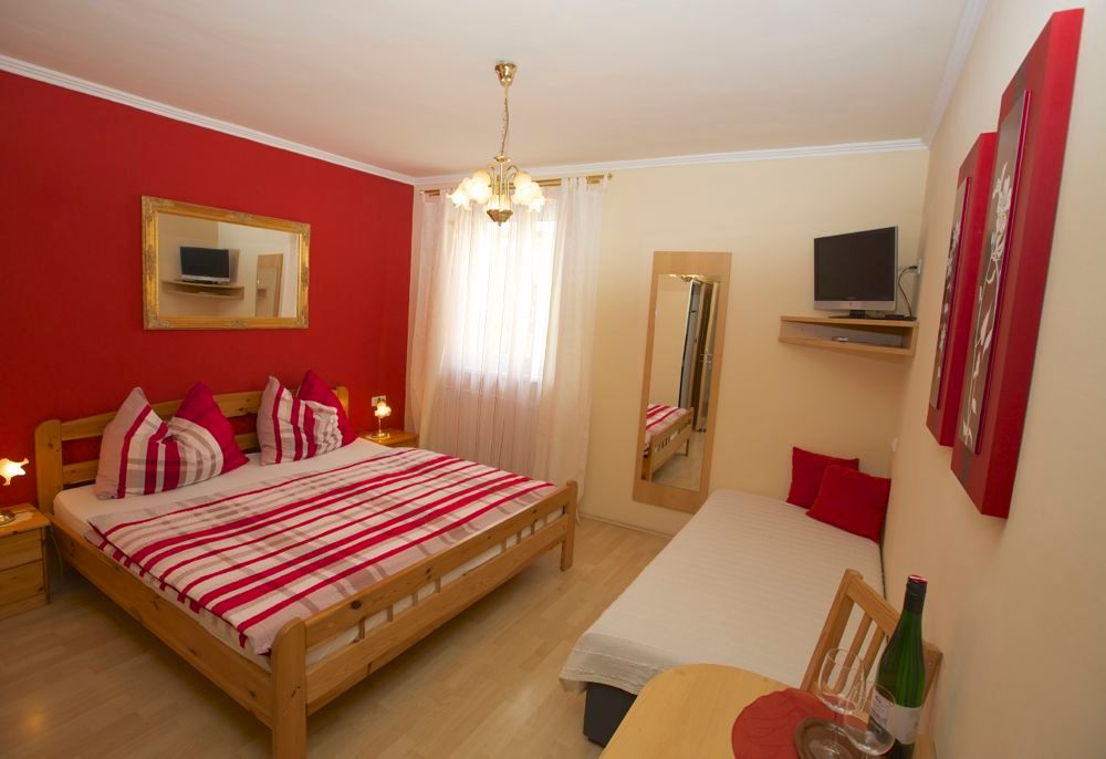 Cozy room with double bed, single bed, red accent wall and TV.