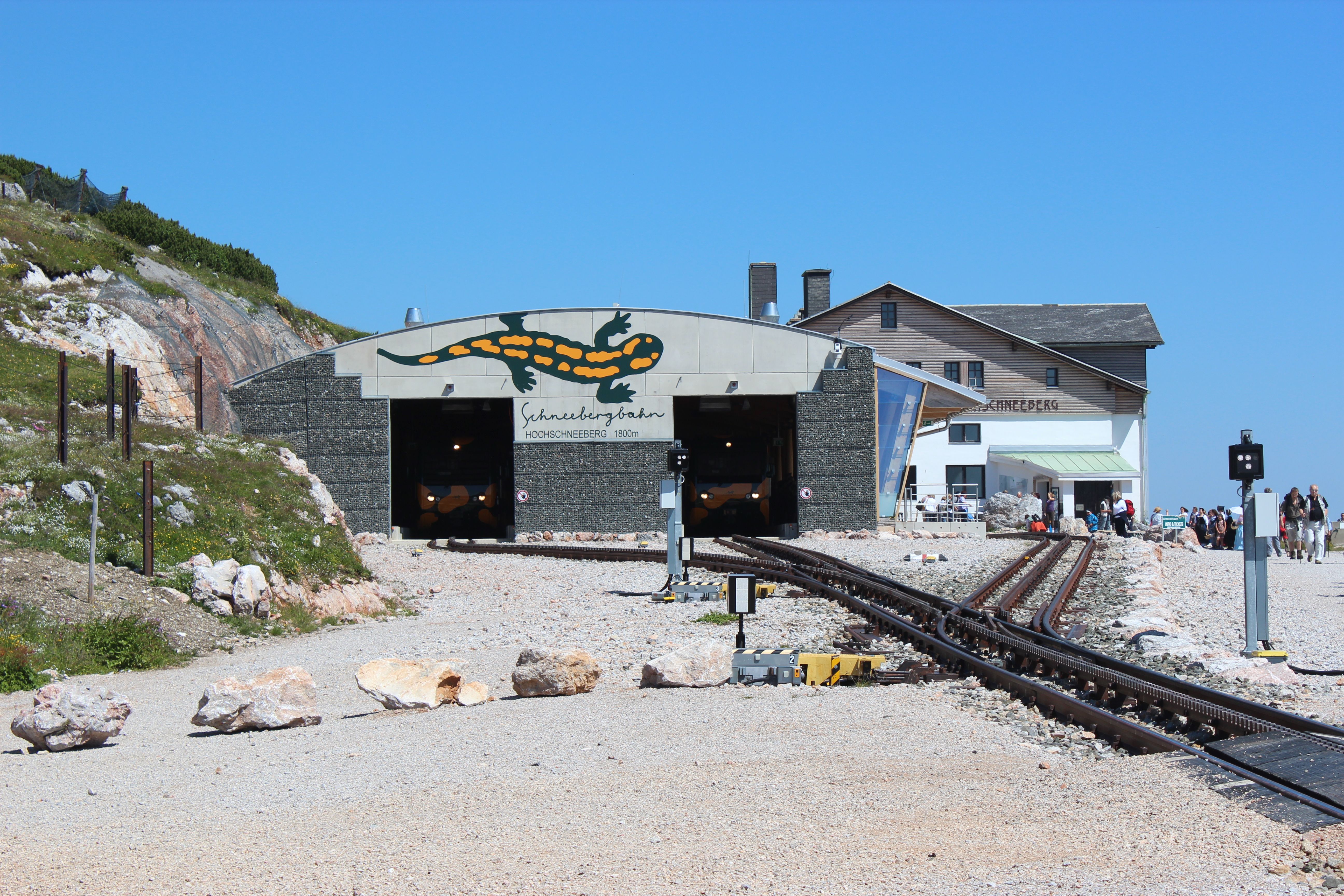 Entrance to the Schneebergbahn with Salamander logo and mountain lodge in the background.