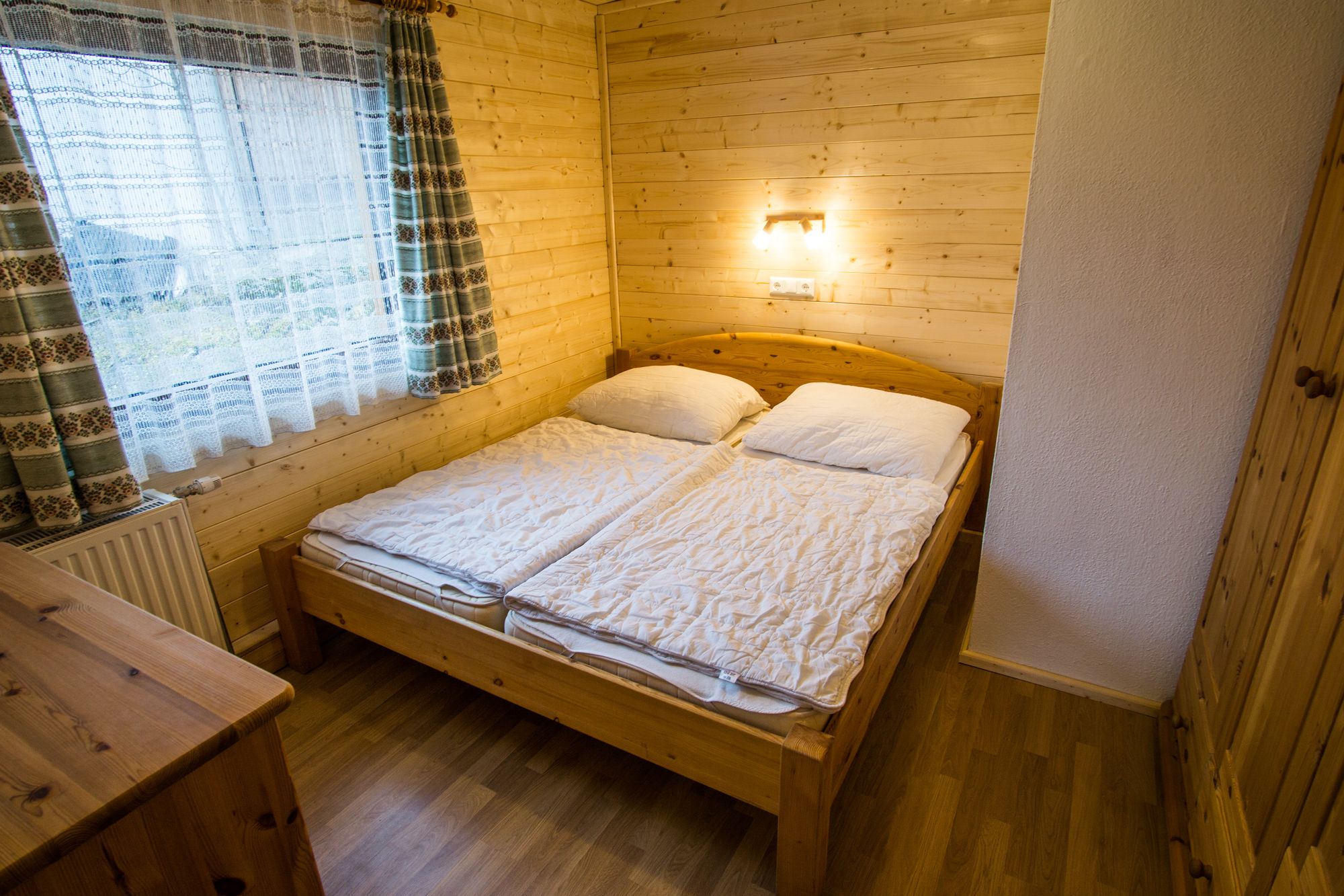 Cozy bedroom with wooden walls, double bed and window with curtains.