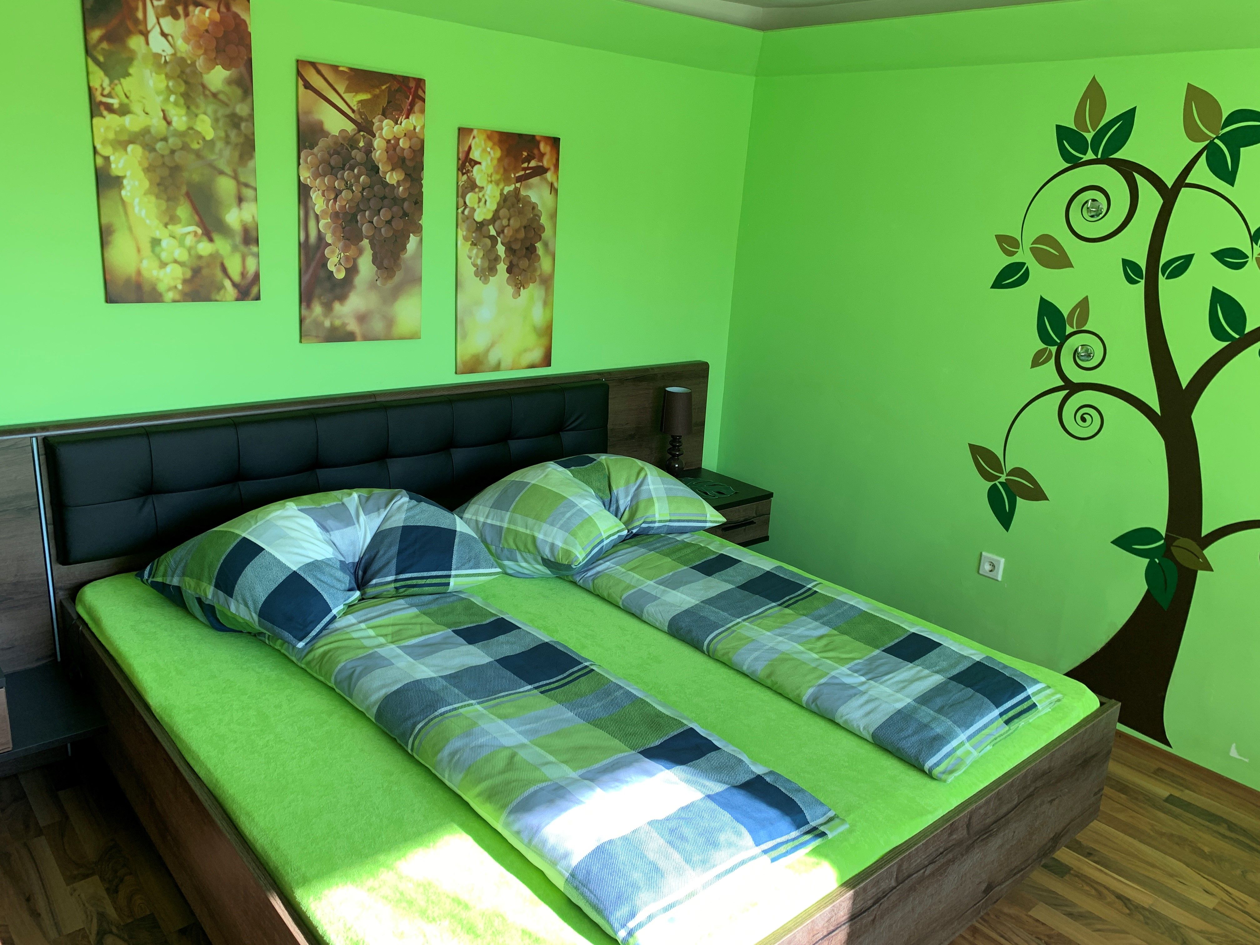 Bedroom with green theme, double bed, murals of grapes and tree decoration.