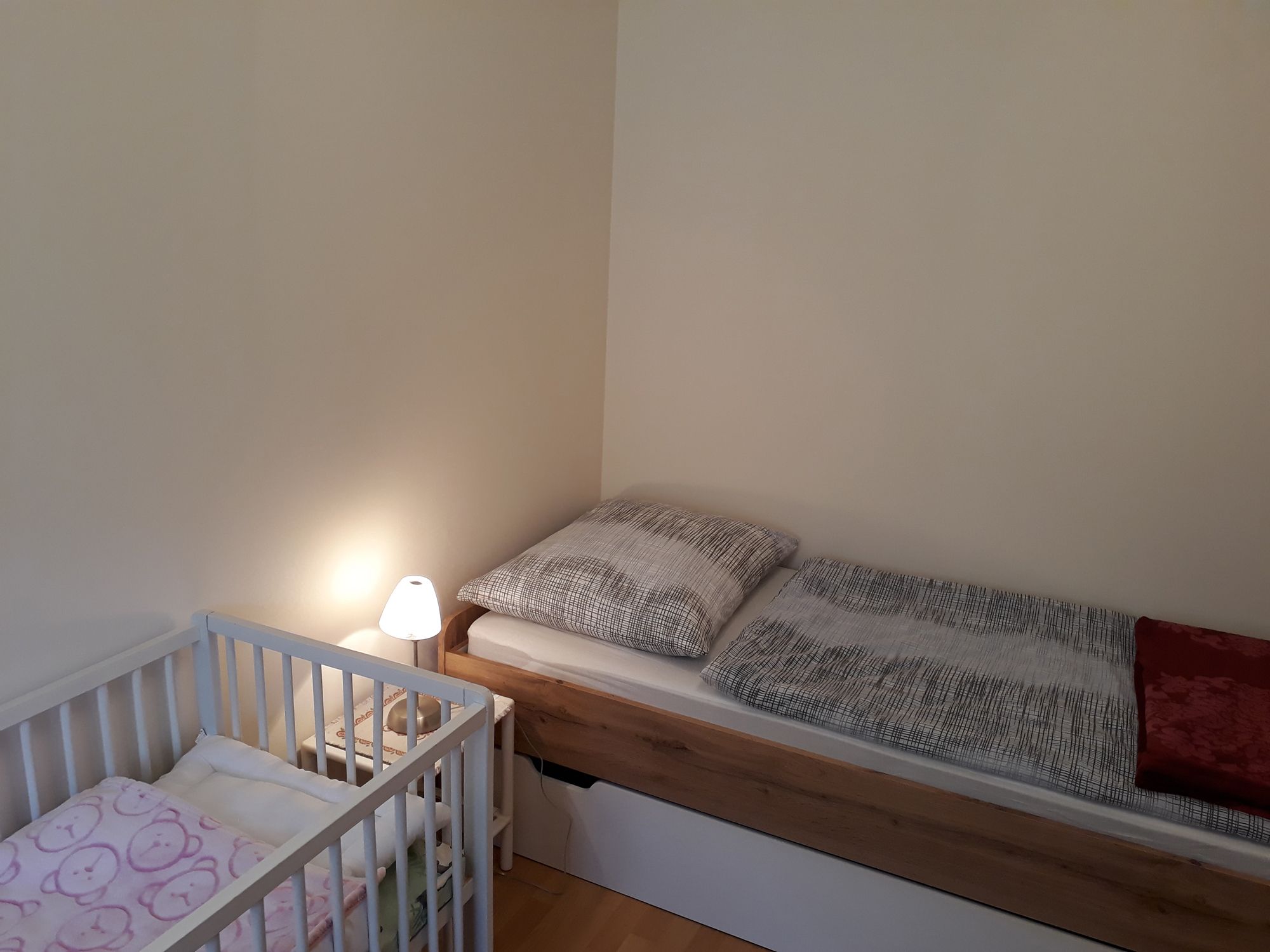 Single room with single bed, crib and bedside lamp.