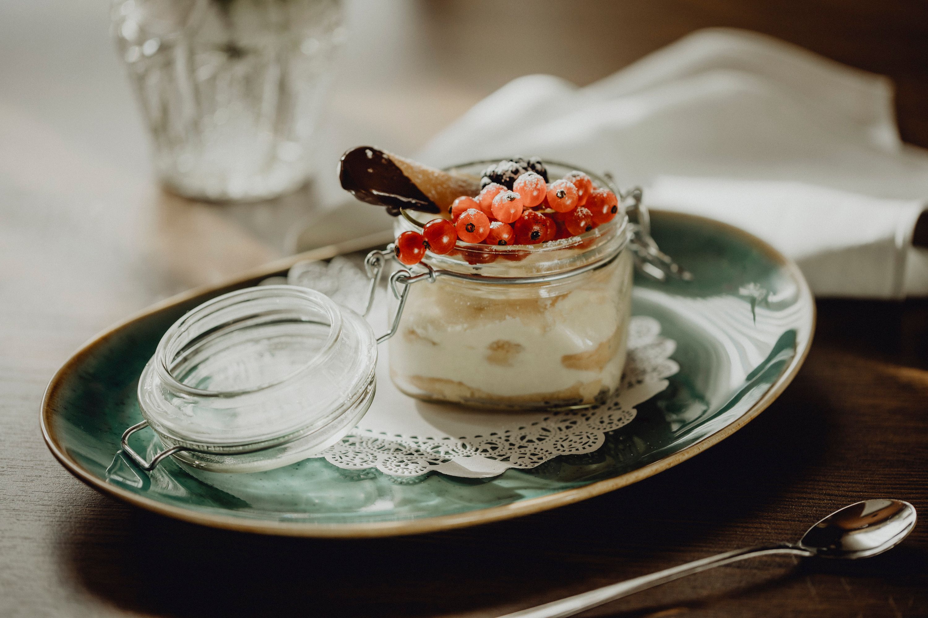 Dessert in a glass with red currants and chocolate cookie on a green plate.