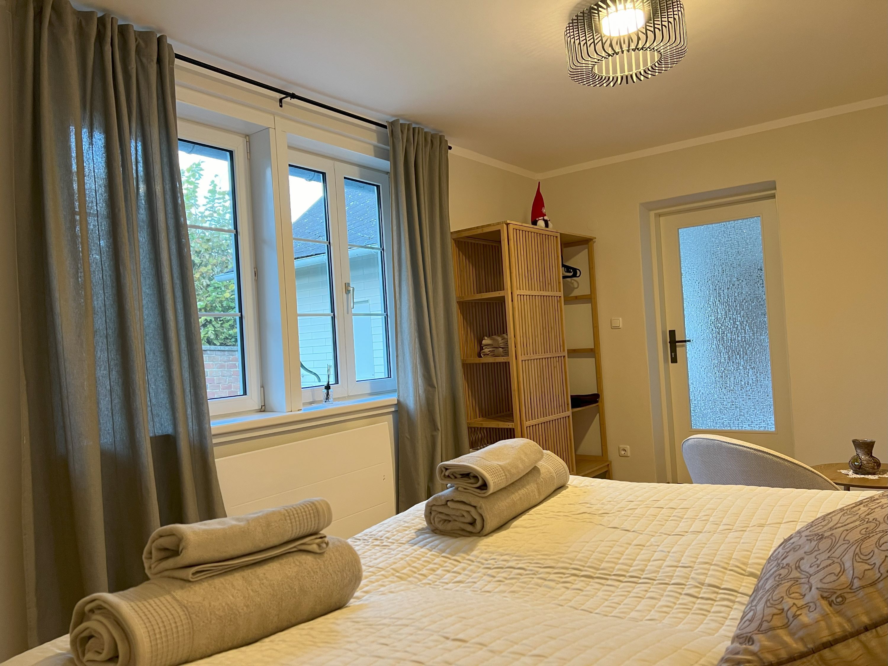 A cozy bedroom with a bed with towels on it, a window with curtains and a shelf with decorations.
