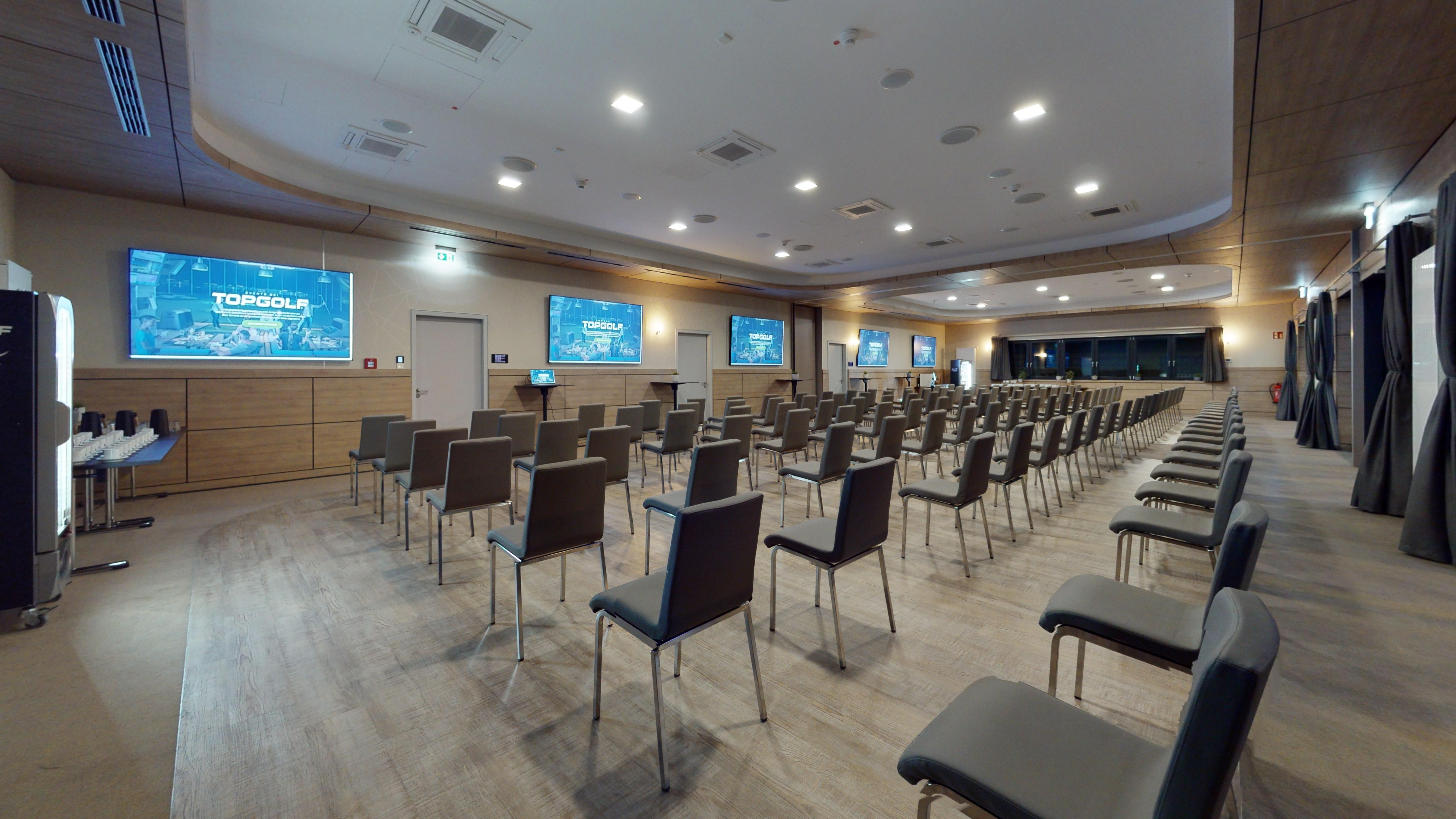 An empty seminar room with rows of chairs and screens on the walls.