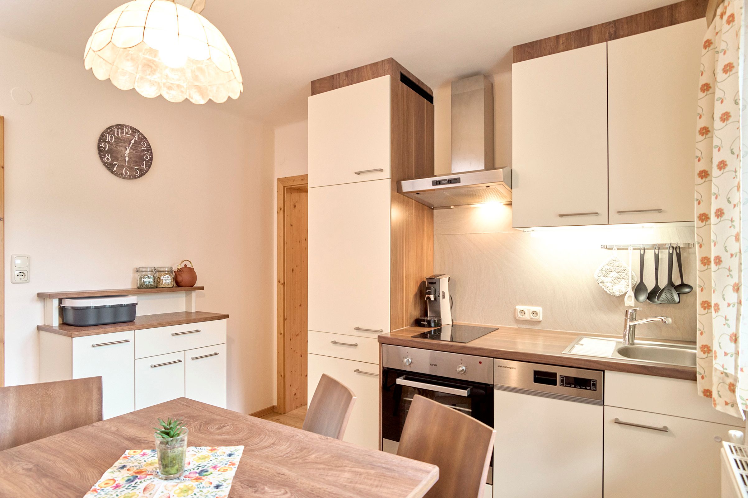 Modern kitchen with wood and white tones, dining table, hanging lamp and kitchen appliances.