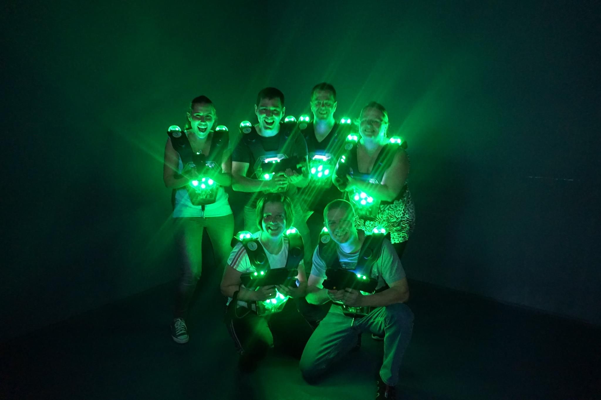 Group of six people in laser tag equipment with green lights in a dark room.