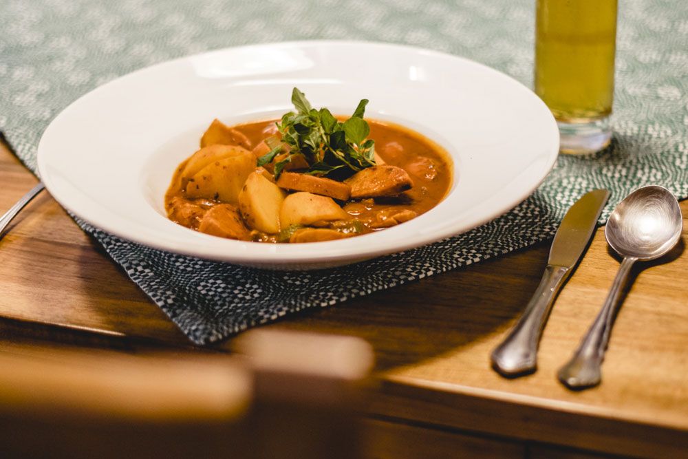 A plate of potato goulash on a table, cutlery and a glass of drink next to it.