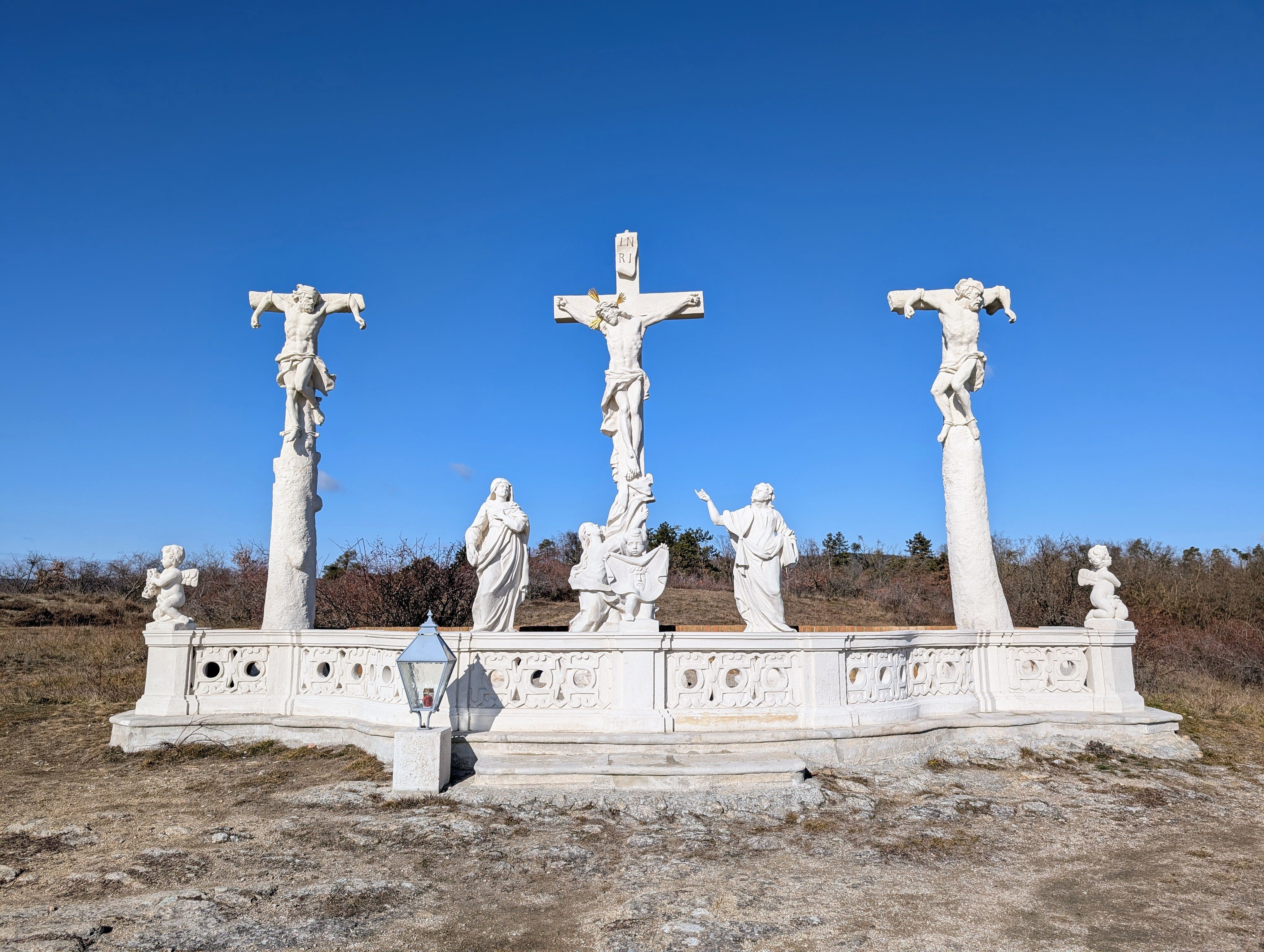 Calvary with three crosses and statues against a blue sky.