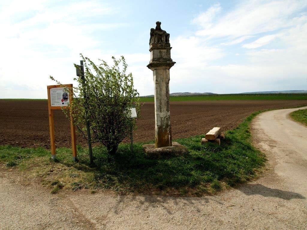 Stone pillar next to a field path with information board and bushes.