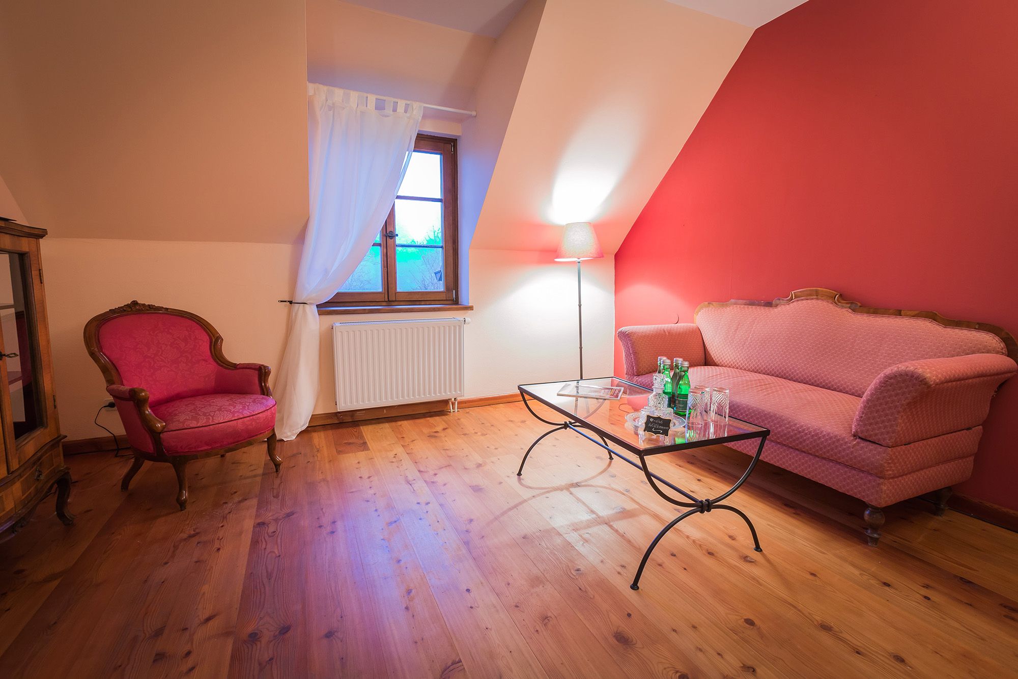 Cozy living room with red sofa, armchair, glass table and floor lamp in front of a red wall.