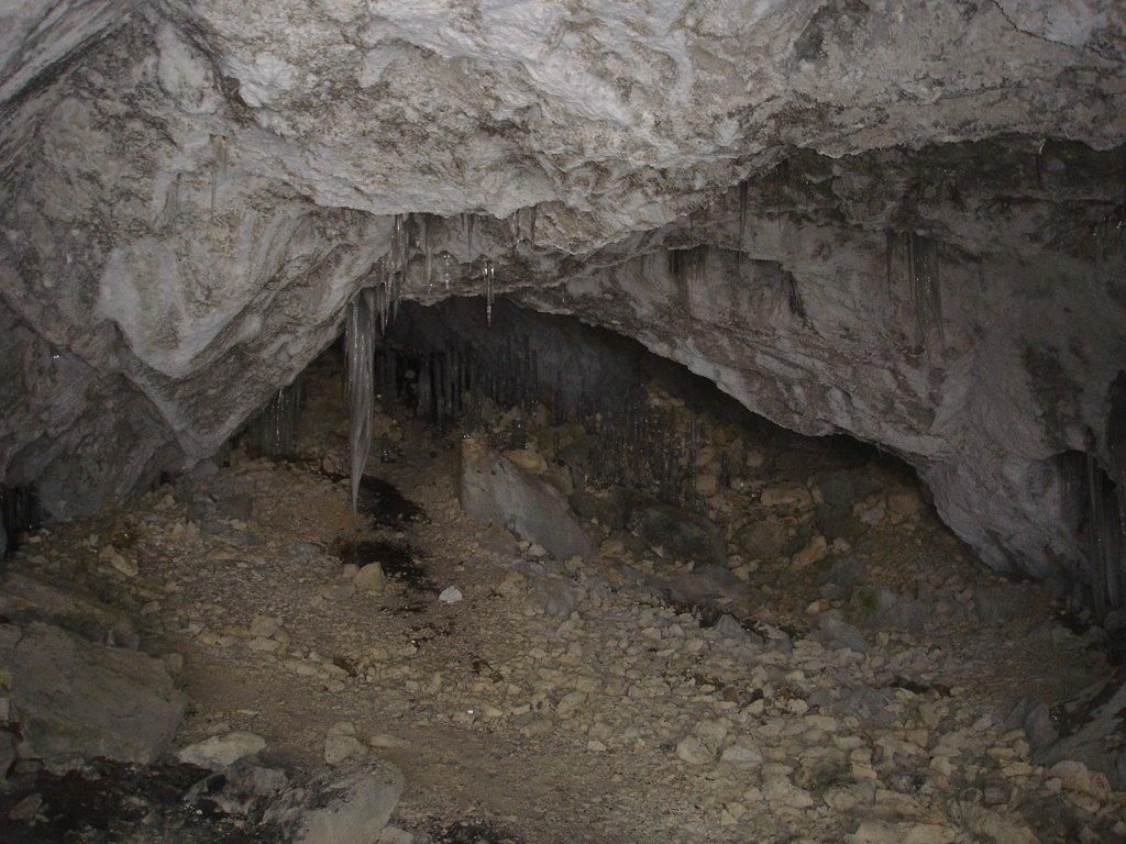 Interior view of a dry cave with stalactites and a stony floor.
