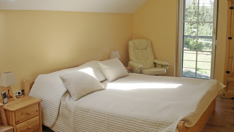 Bright bedroom with double bed, armchair and window with a view of the greenery.