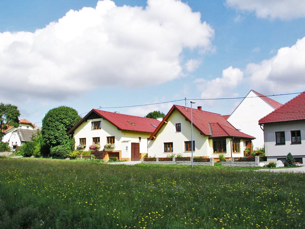 An organic farm with several yellow buildings and red roofs, surrounded by green meadows and trees under a blue sky with clouds.