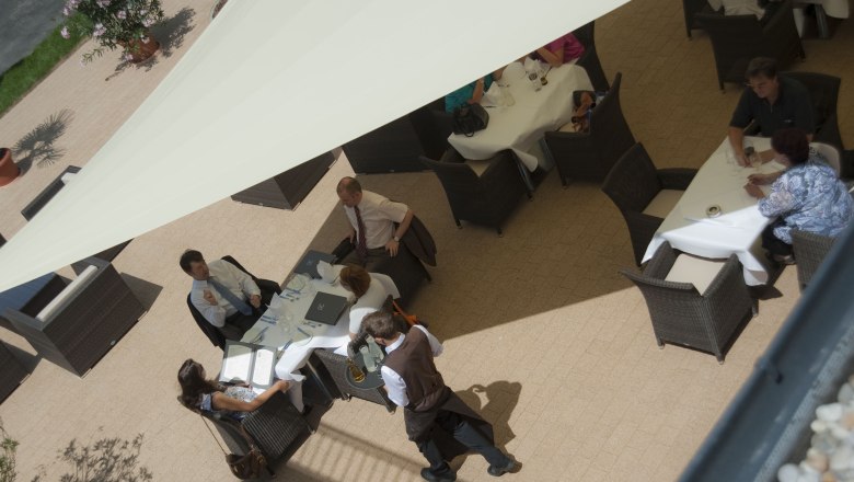 Aerial view of a hotel terrace with guests at tables under an awning.