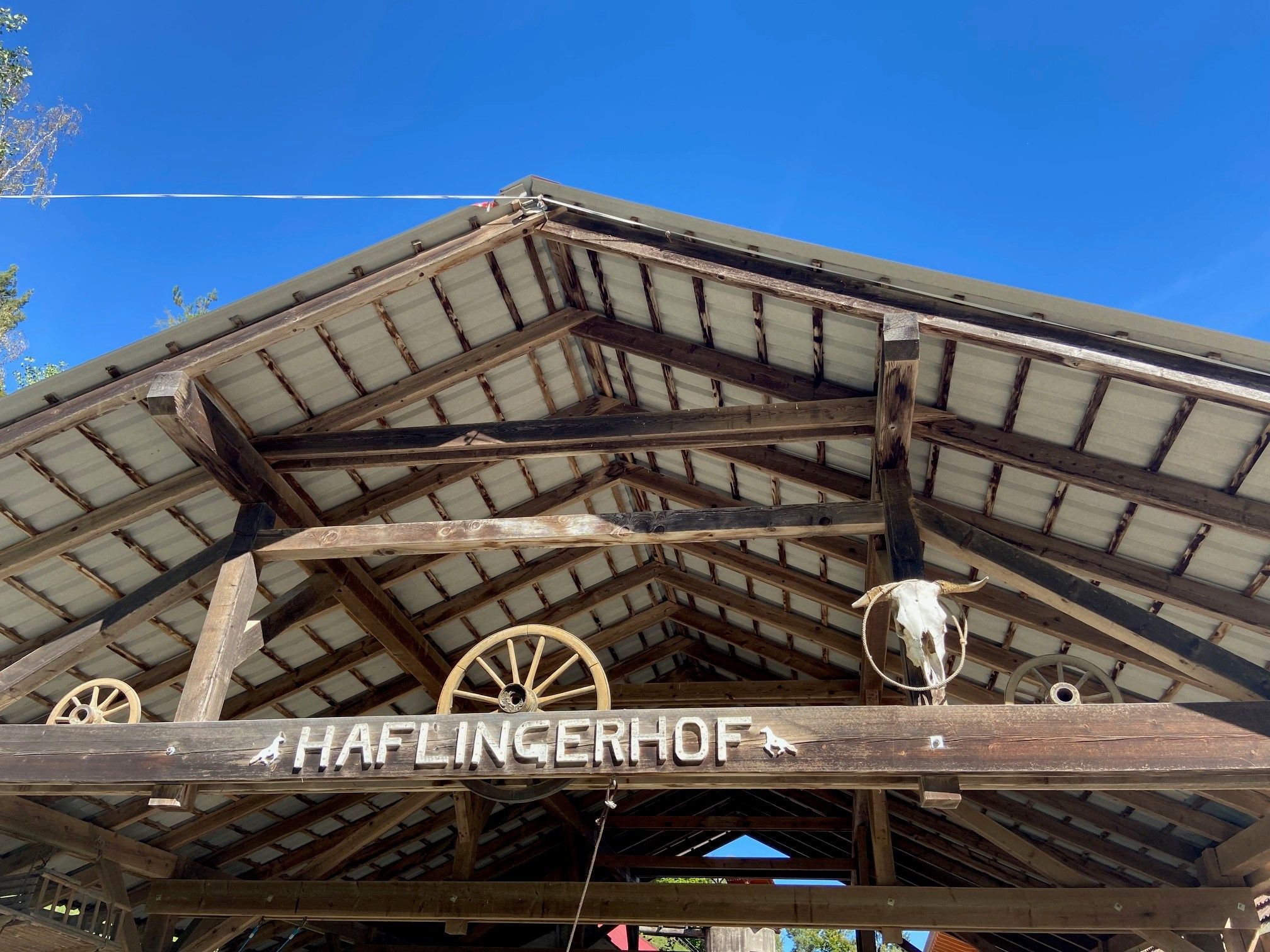 Roof of a wooden building with the lettering 'Haflingerhof' and decorations such as wagon wheels and an animal head.