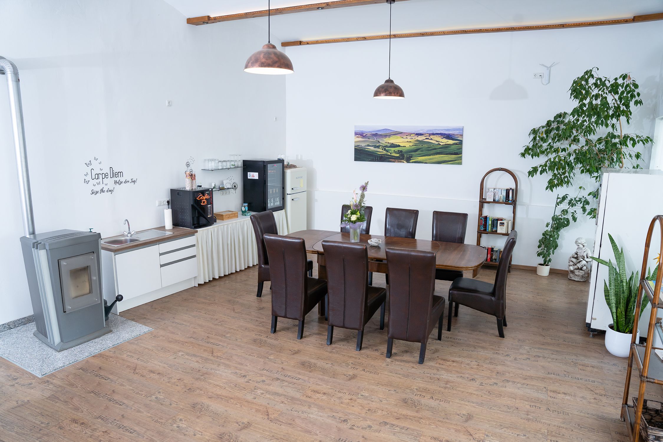 Cozy room with dining table, chairs, plants and kitchenette.