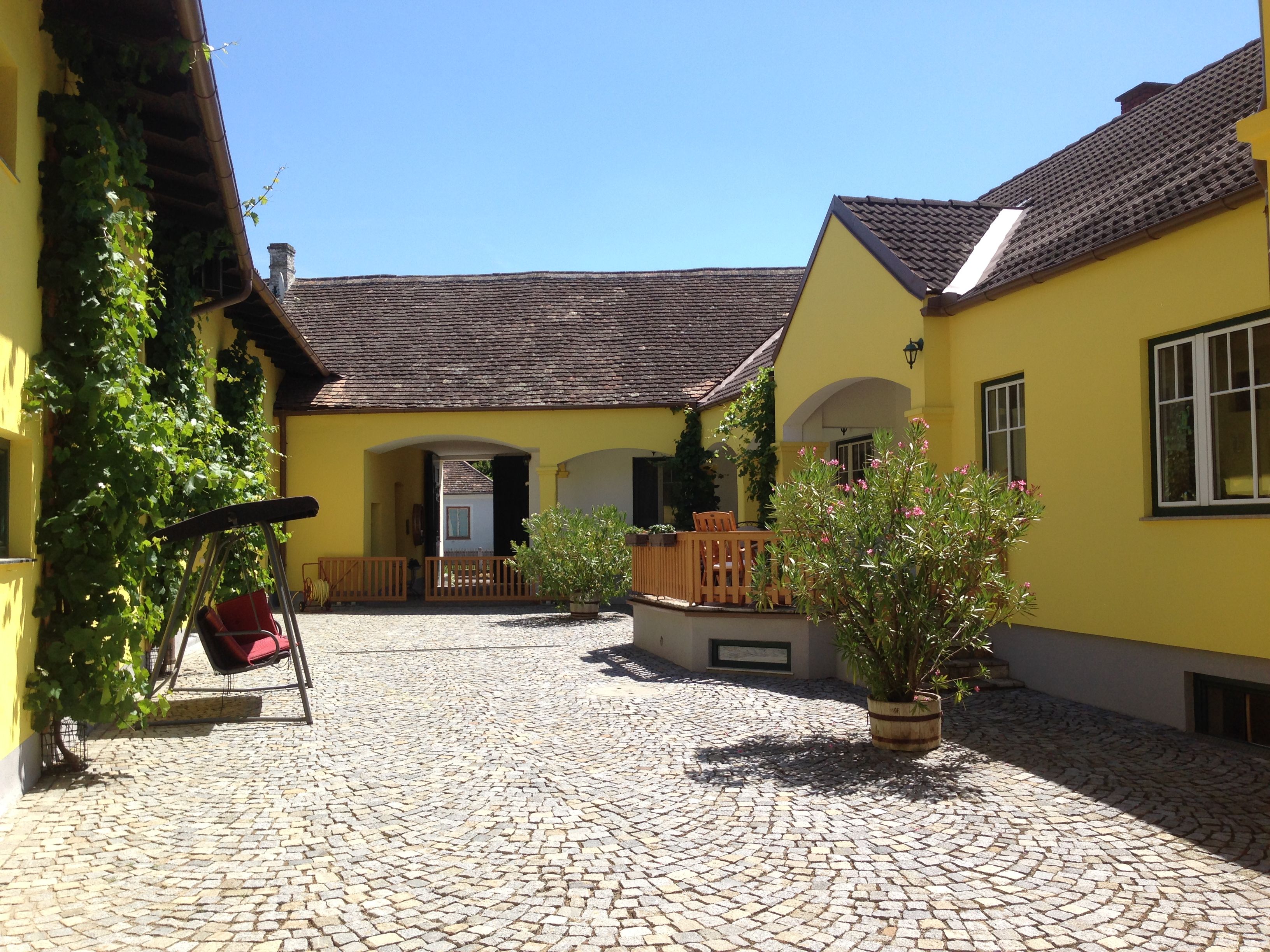 Inner courtyard of a yellow vineyard with cobblestones, swing and plants.