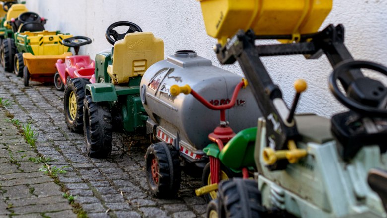 Row of toy tractors on a white wall on cobblestones.