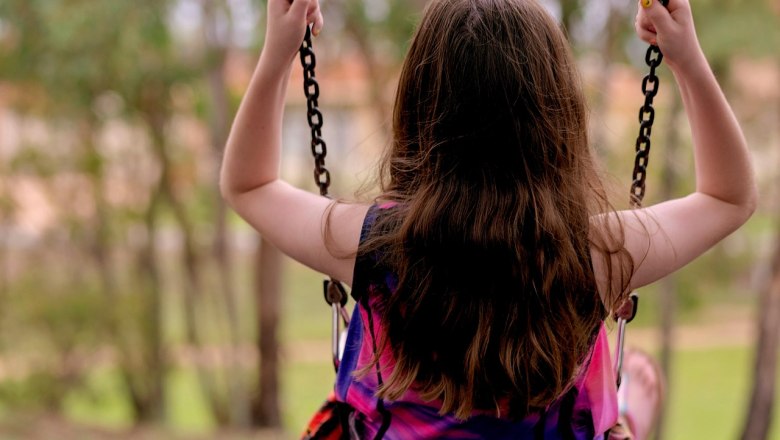 A child swings on a swing outdoors, surrounded by trees.