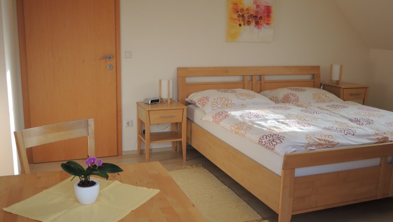 A guest room with a double bed, two bedside tables, a table and chair and a potted plant.