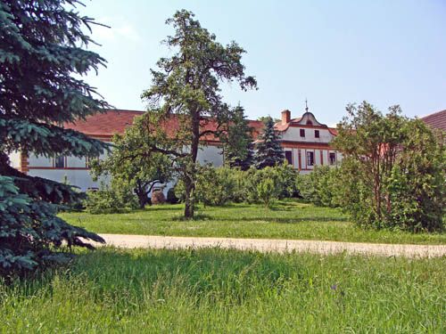 A historic building with a red roof, surrounded by trees and a green meadow.