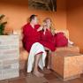 A couple in red bathrobes clink glasses of champagne in a sauna and relaxation area.