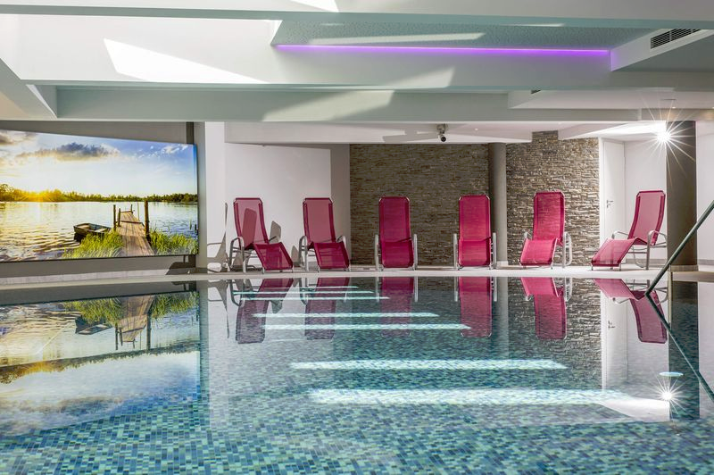 Indoor pool with red deckchairs, stone walls and a large mural.