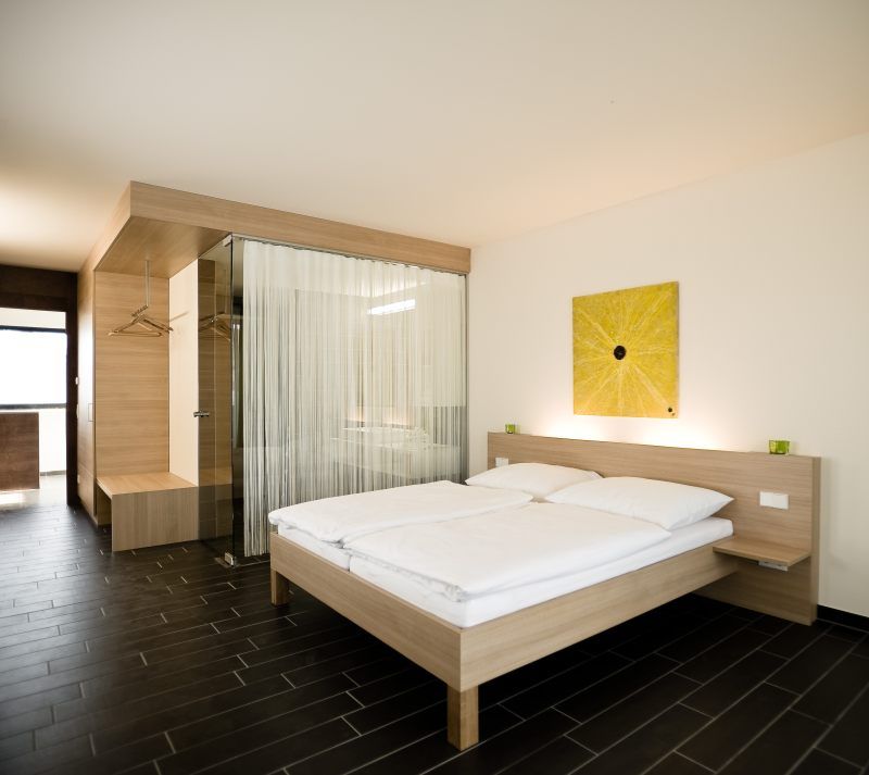 Modern hotel room with double bed, wooden furniture and glass wall.