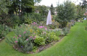 A cottage garden with colorful flowers, a closed sunshade and a well-tended lawn.